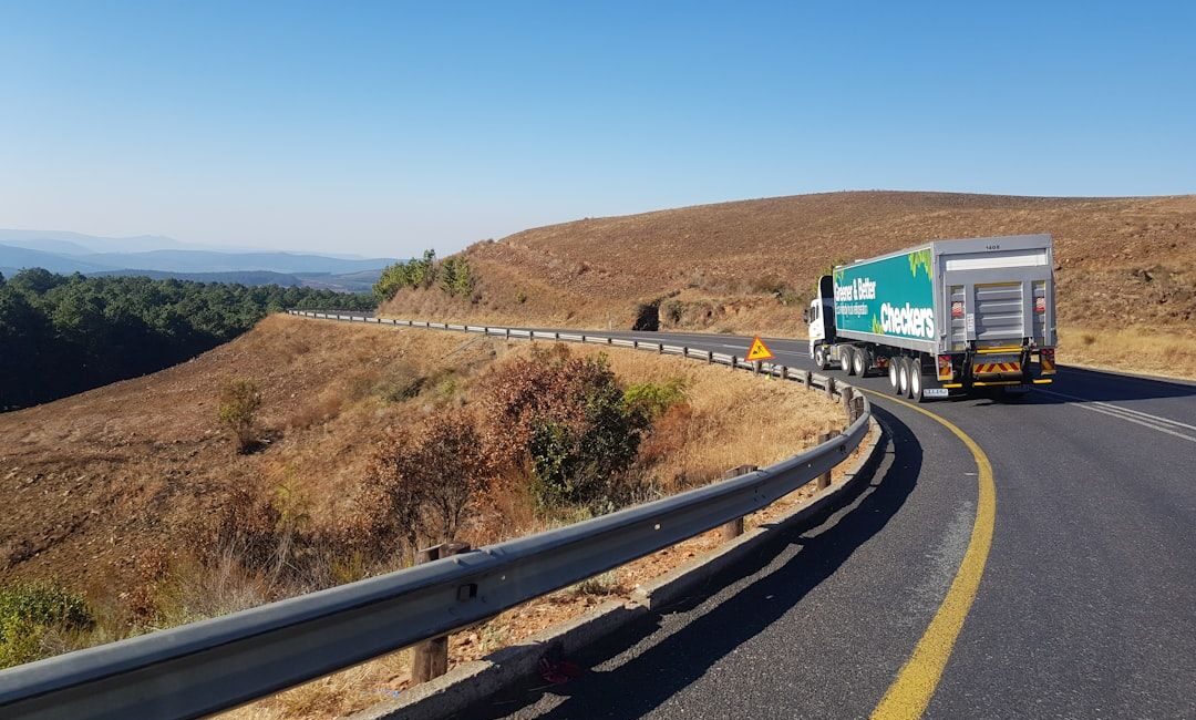A green Checkers delivery truck driving on a winding road through dry hills