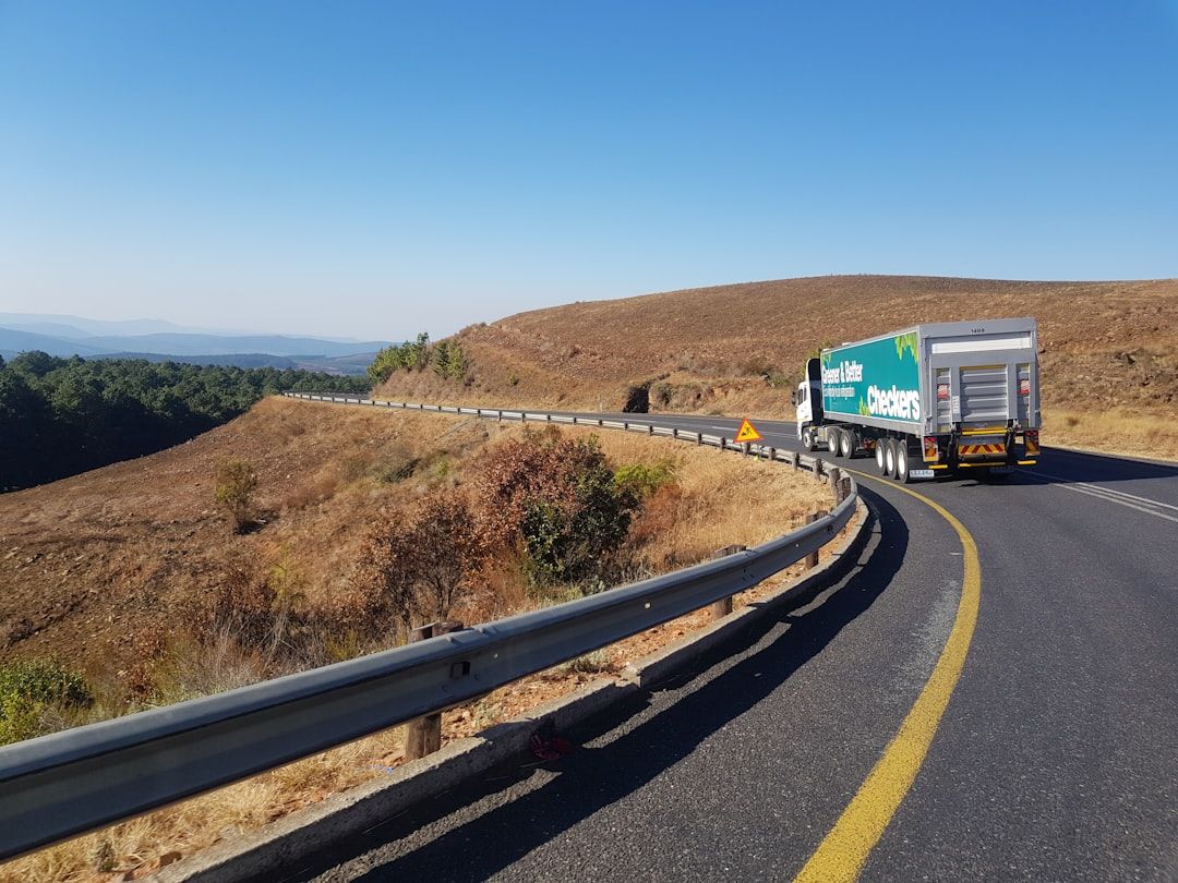 A green Checkers delivery truck driving on a winding road through dry hills